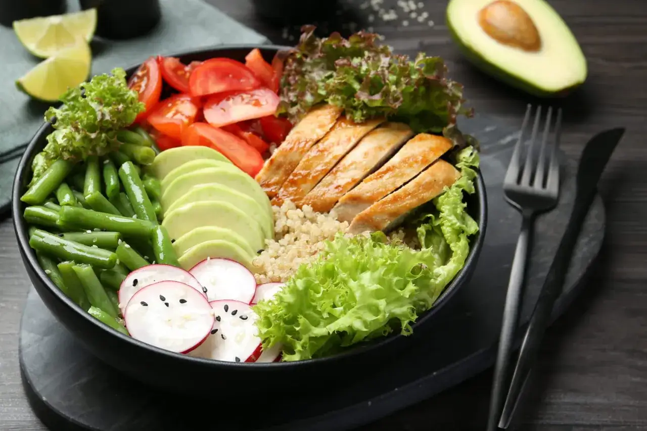Un bol coloré avec poulet grillé, avocat, haricots verts, tomates, radis et quinoa. Un repas sain et un menu équilibré pour une alimentation savoureuse.