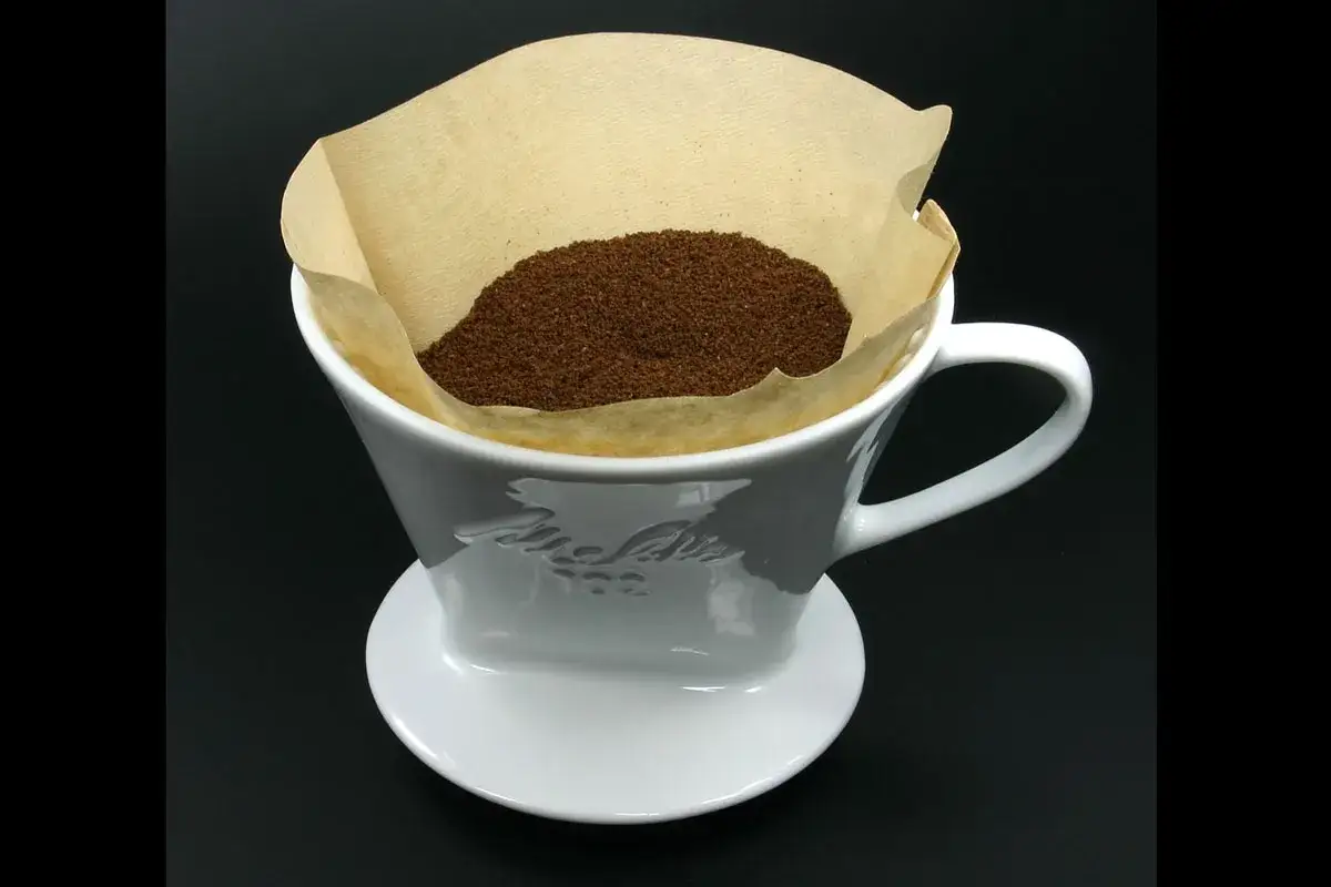 En vit kaffefilterh&aring;llare med kaffepulver i ett pappersfilter. Enkelheten i designen p&aring;minner om vem som uppfann kaffefiltret.