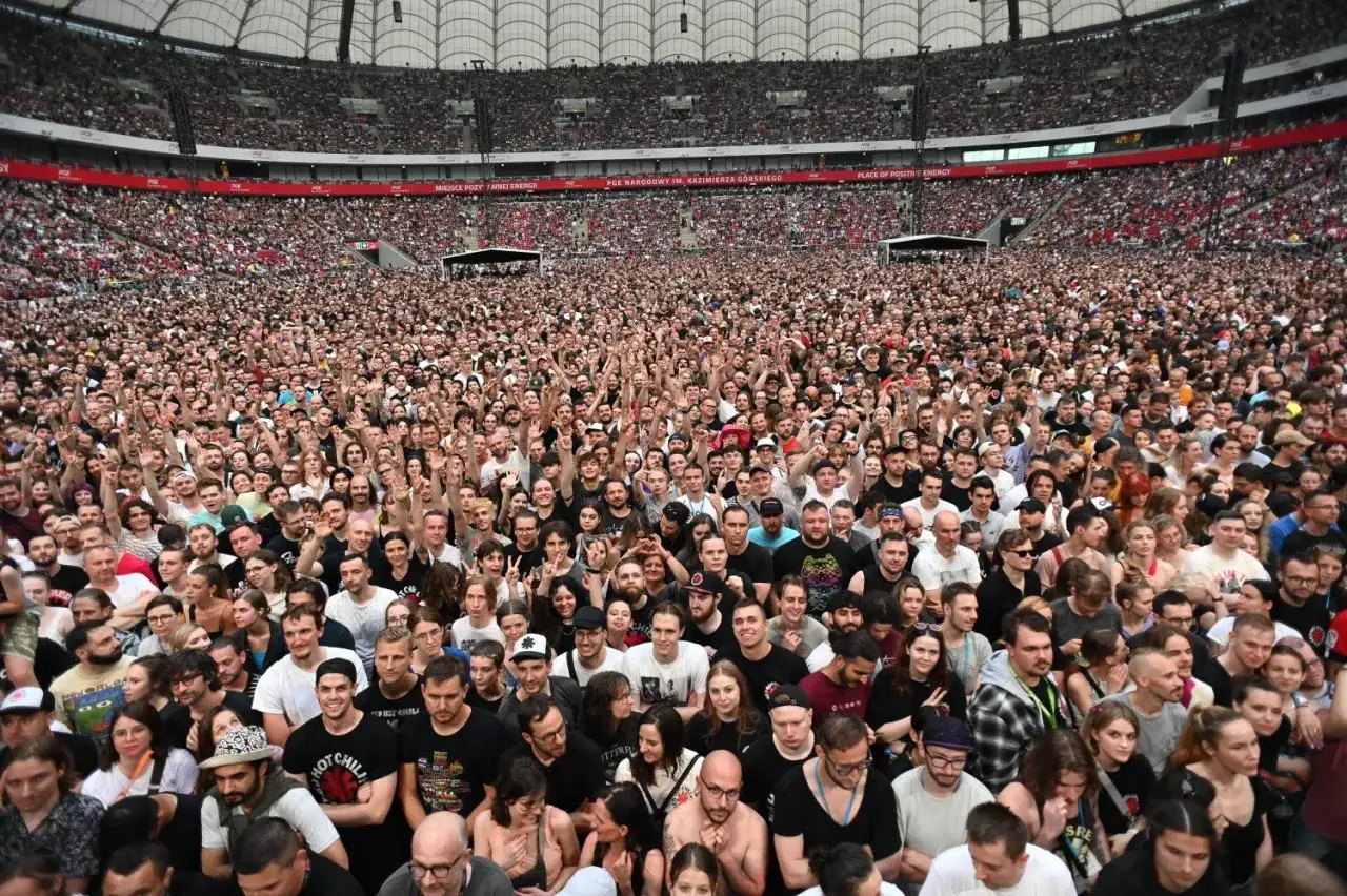 Tłum fanów na koncercie Red Hot Chili Peppers w Warszawie. Stadion PGE Narodowy wypełniony po brzegi, ludzie wznoszą ręce w geście radości.