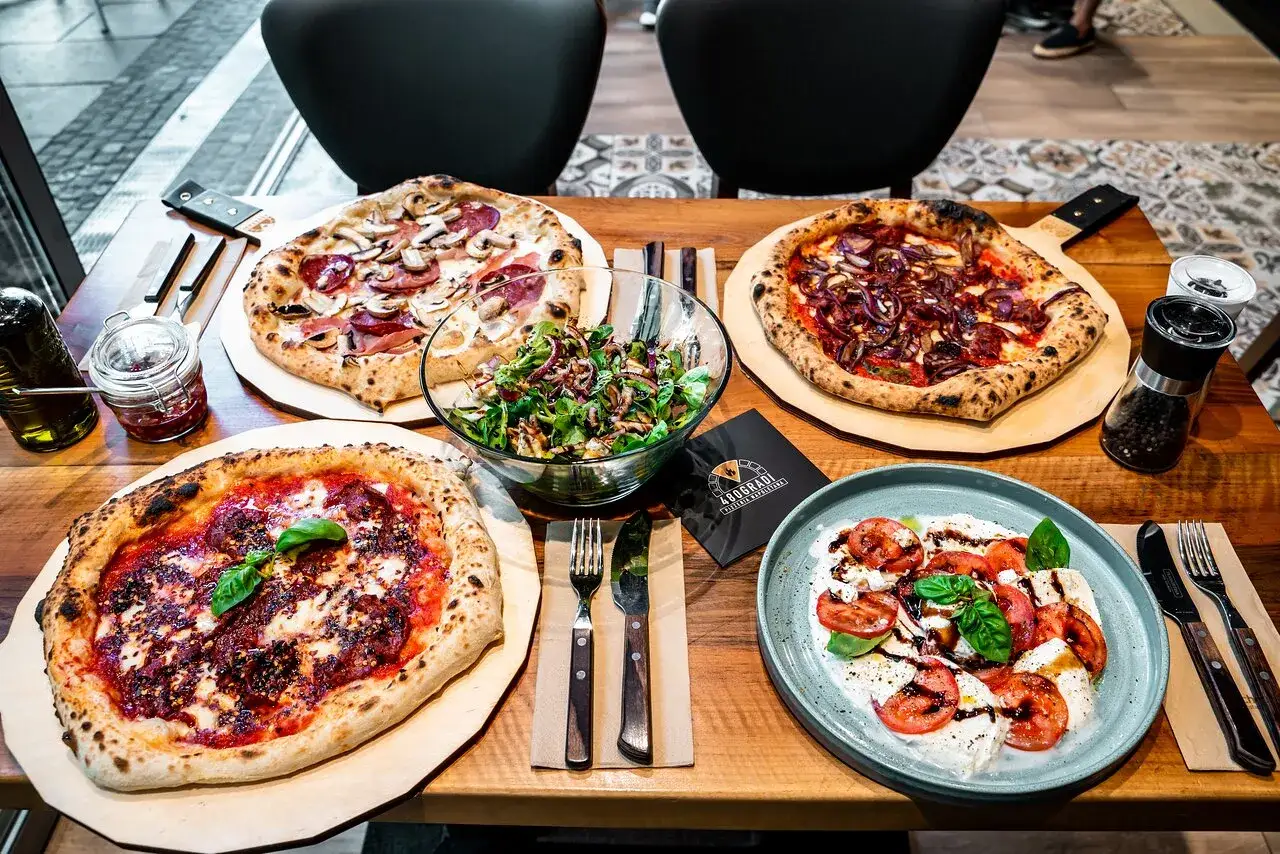 Drei neapolitanische Pizzen, ein Salat und Caprese-Salat auf einem Holztisch. Die neapolitanische Pizza Temperatur ist perfekt für den Genuss.