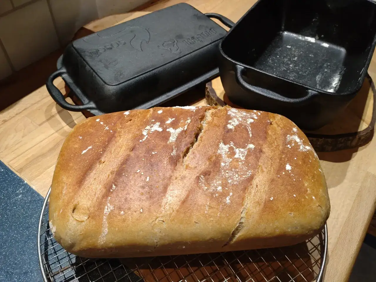 Frisch gebackenes Brot auf einem Gitter, daneben zwei Gusseisenformen – perfekt für das nächste Brot selber backen!