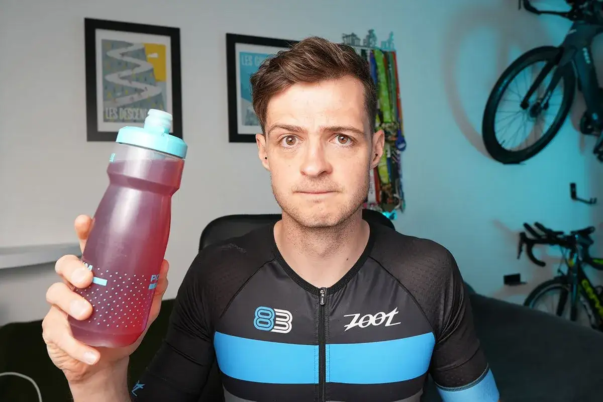 Un athl&egrave;te en tenue de cyclisme tient une gourde rose. Il discute de la nutrition Ironman, essentiel pour la performance.