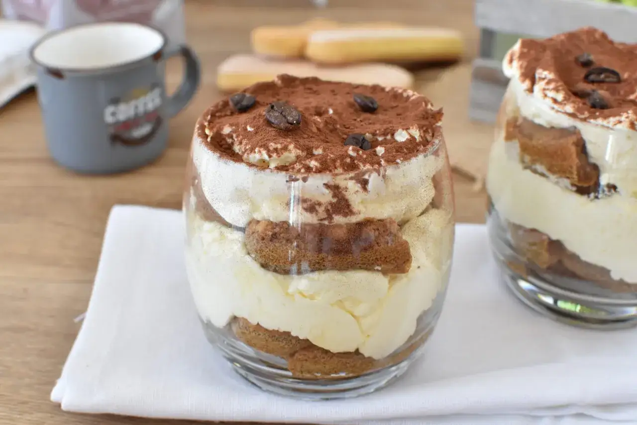 Delizioso dessert in bicchiere: strati di crema e savoiardi inzuppati nel caffè, guarnito con cacao e chicchi di caffè. Perfetto per un momento di piacere.