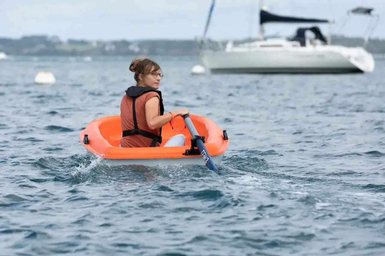Une femme rame dans une petite barque orange, le mot 