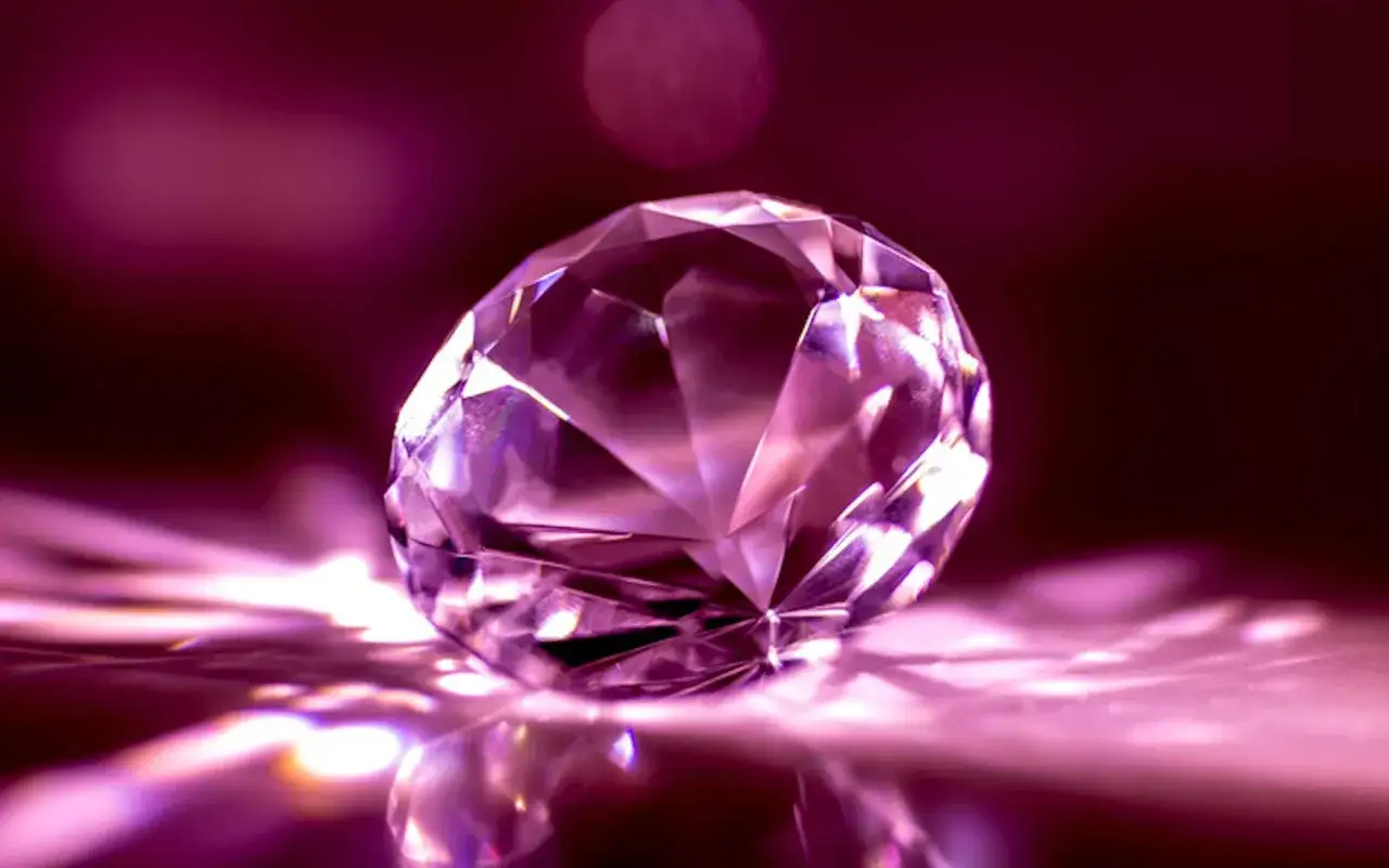 Un magnifico diamante rosa, forse il diamante pi&ugrave; costoso al mondo, brilla su una superficie riflettente, catturando la luce.