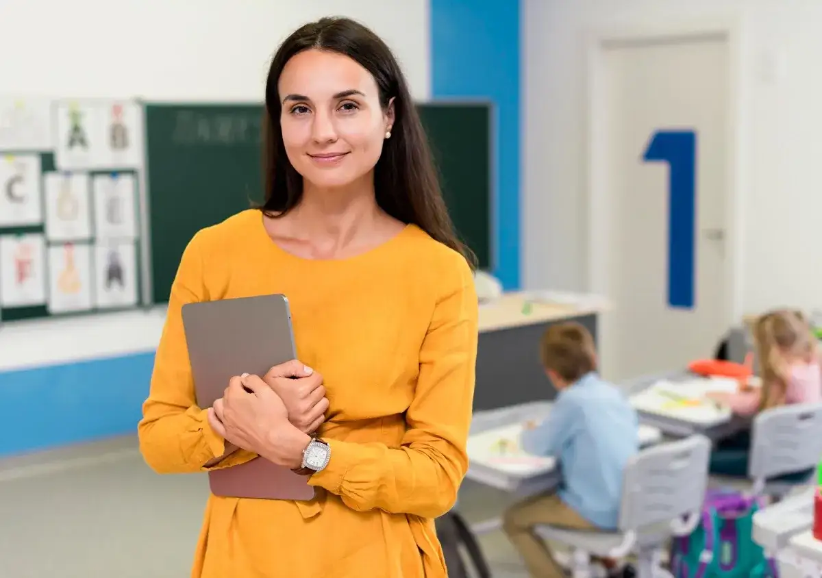 Nauczycielka z tabletem w sali lekcyjnej, przygotowująca się do zajęć. Jej pasja do pracy z dziećmi znajduje odzwierciedlenie w jej zaangażowaniu w studia podyplomowe nauczyciel wspomagający.