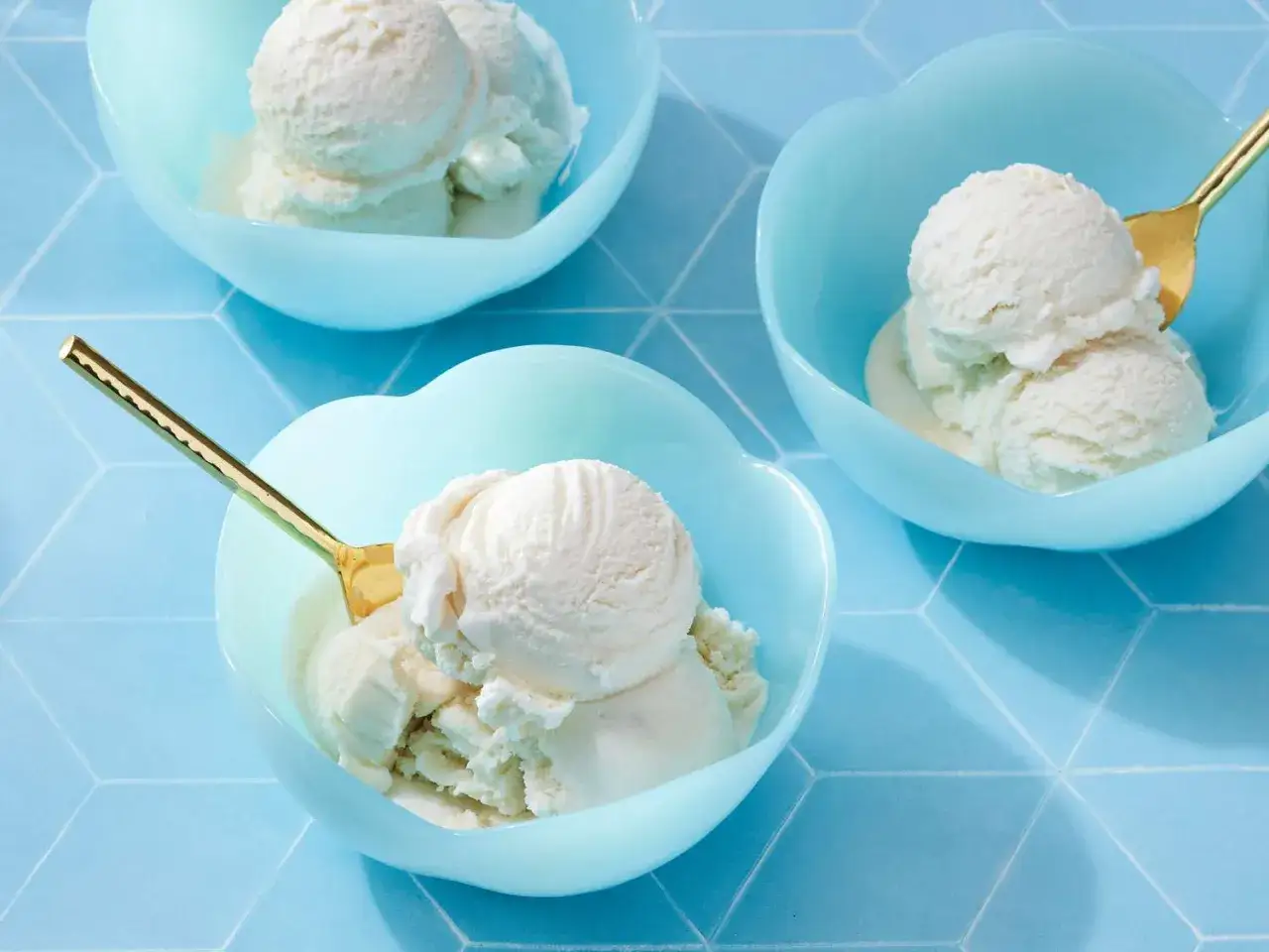 Cremiges selbstgemachtes Eis in hellblauen Schalen. Goldene Löffel warten darauf, das köstliche Dessert zu genießen.