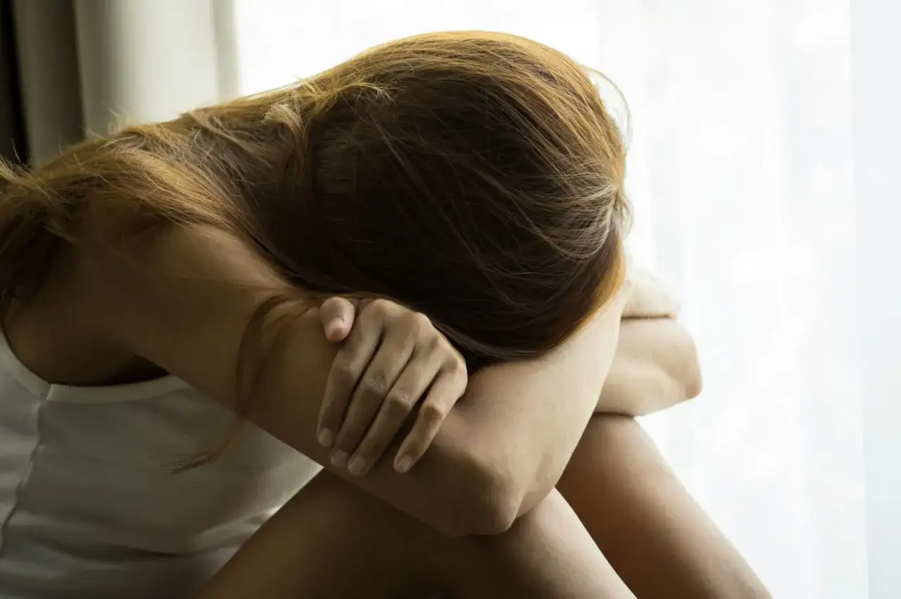 Kobieta skulona, z głową ukrytą w ramionach, odzwierciedla wewnętrzne zmagania i emocjonalne napięcie, typowe dla osób neurotycznych.