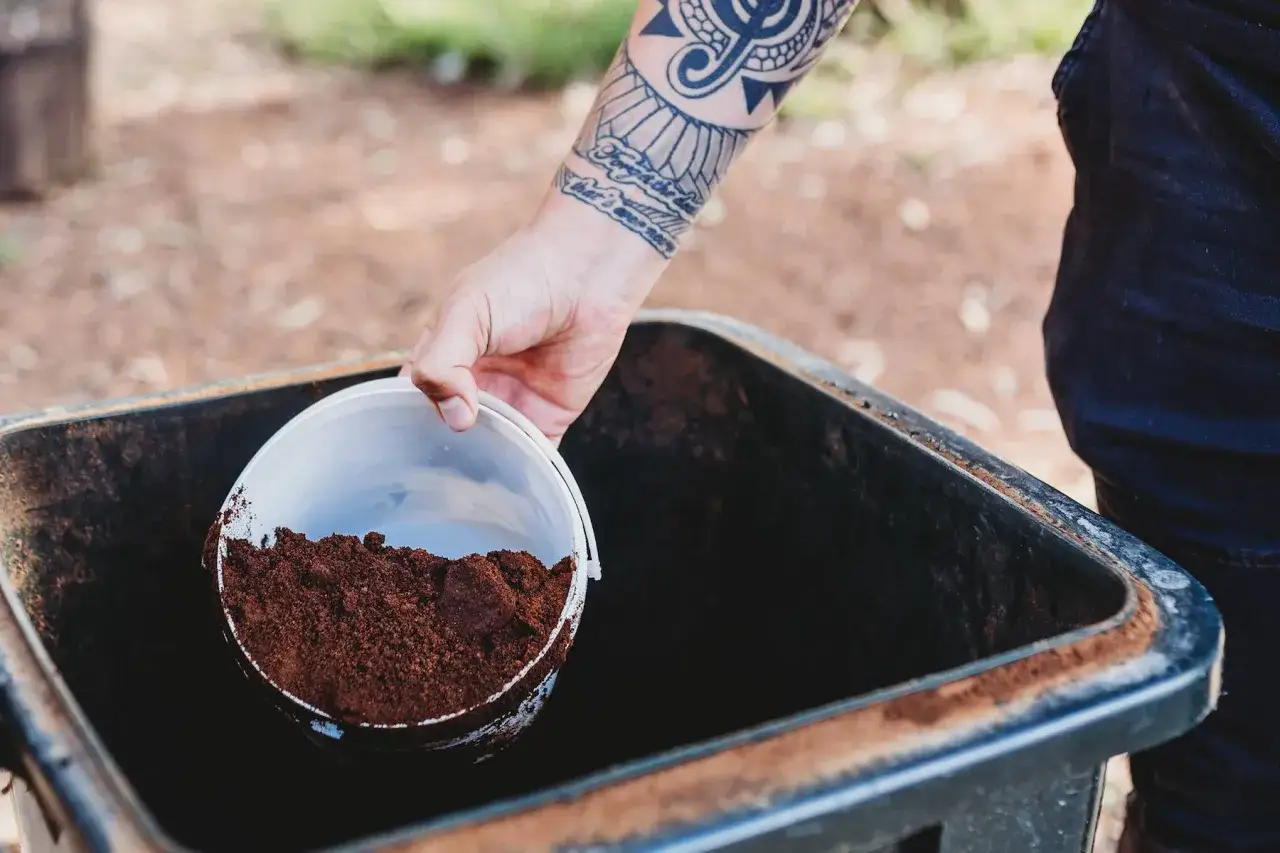 Mano con tatuaje vierte posos de café en un contenedor.