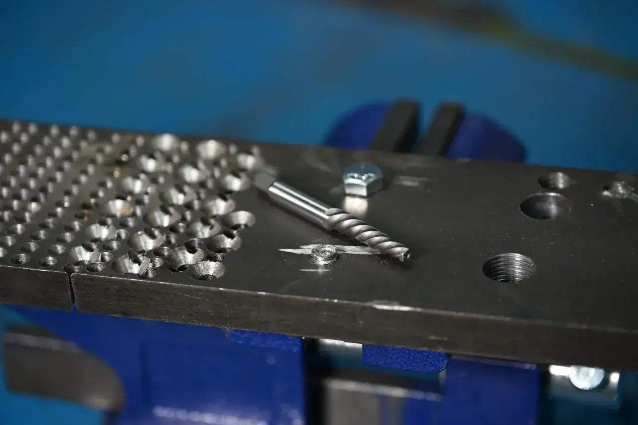 Herramienta para quitar un tornillo pasado de rosca en metal. Tornillo da&ntilde;ado y extractor en una placa met&aacute;lica sujeta en un tornillo de banco.
