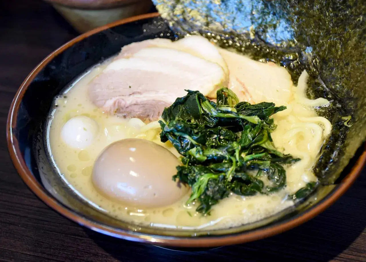 Miseczka ramenu z makaronem, plastrami wieprzowiny, zielonymi warzywami i poł&oacute;wką jajka. Idealne jajko do ramen to klucz do sukcesu.
