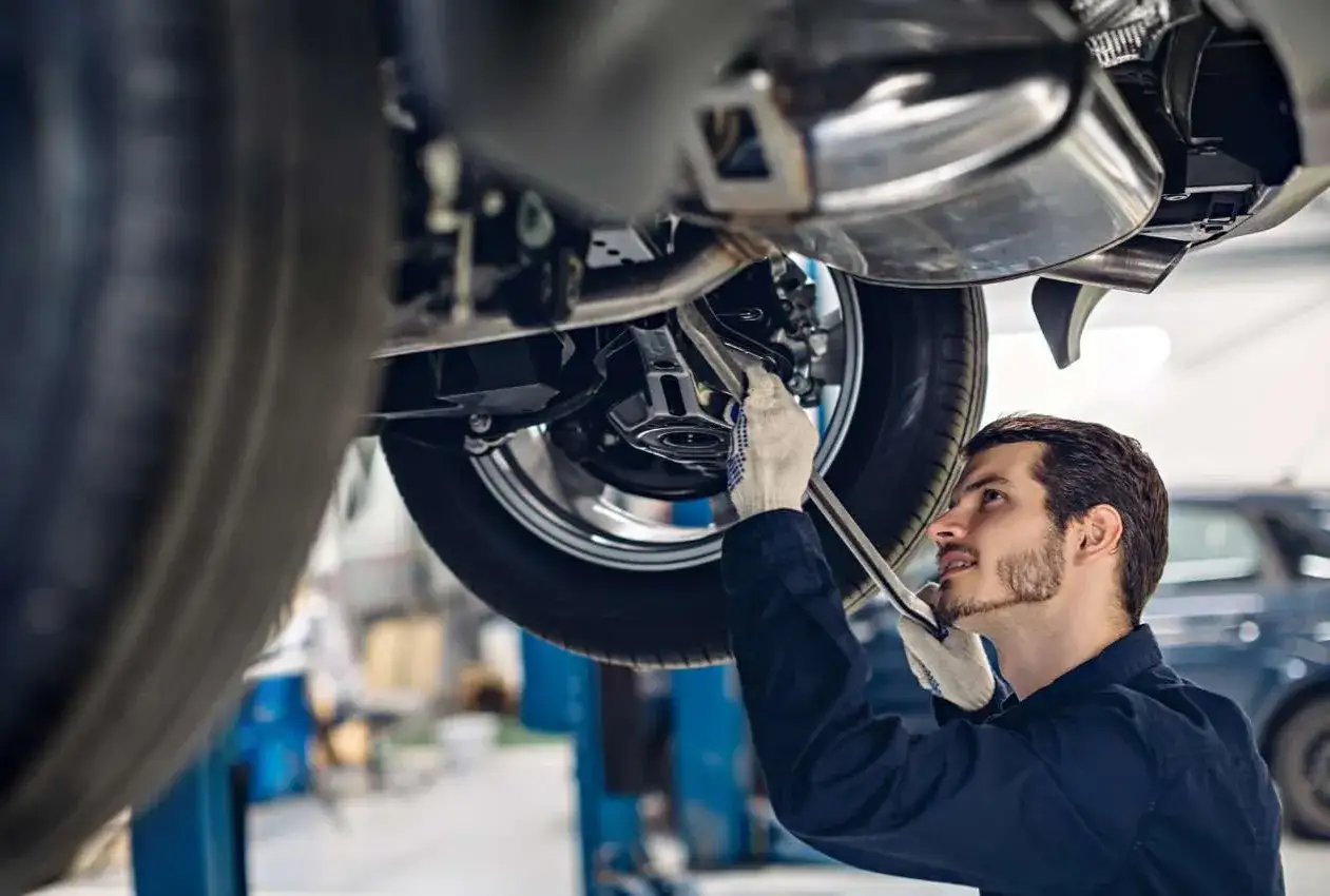 Mechanik w białych rękawiczkach dokręca śrubę przy wielowahaczu zawieszenia samochodu na podnośniku.