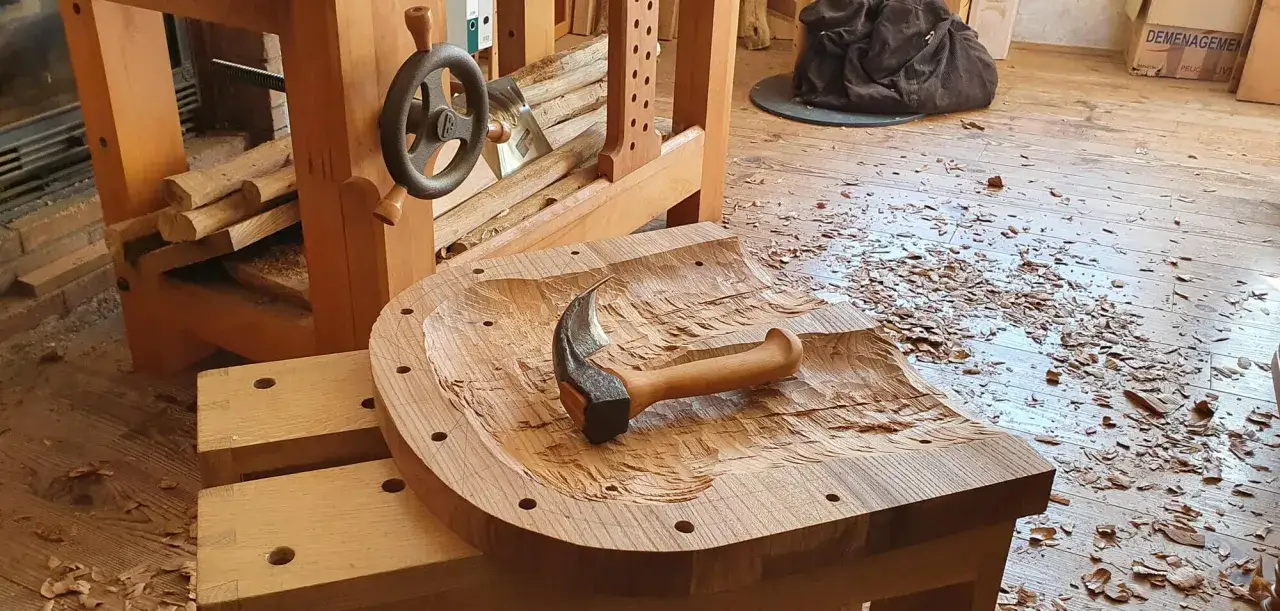 Un marteau repose sur une pi&egrave;ce de bois sculpt&eacute;e, entour&eacute;e de copeaux. Le materiel ebeniste est pr&ecirc;t pour la suite du travail.
