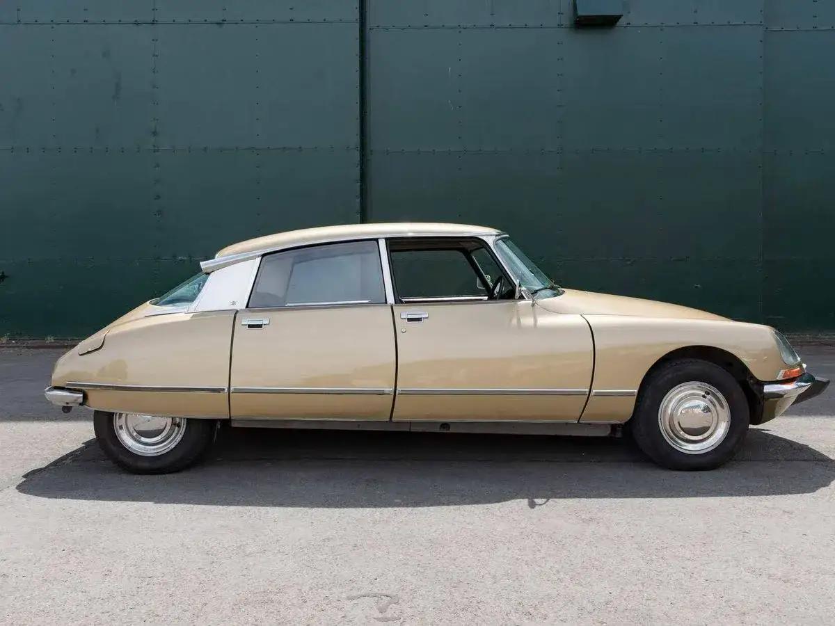Citroën Tiburón beige, un clásico de diseño aerodinámico y futurista, aparcado frente a una pared verde.