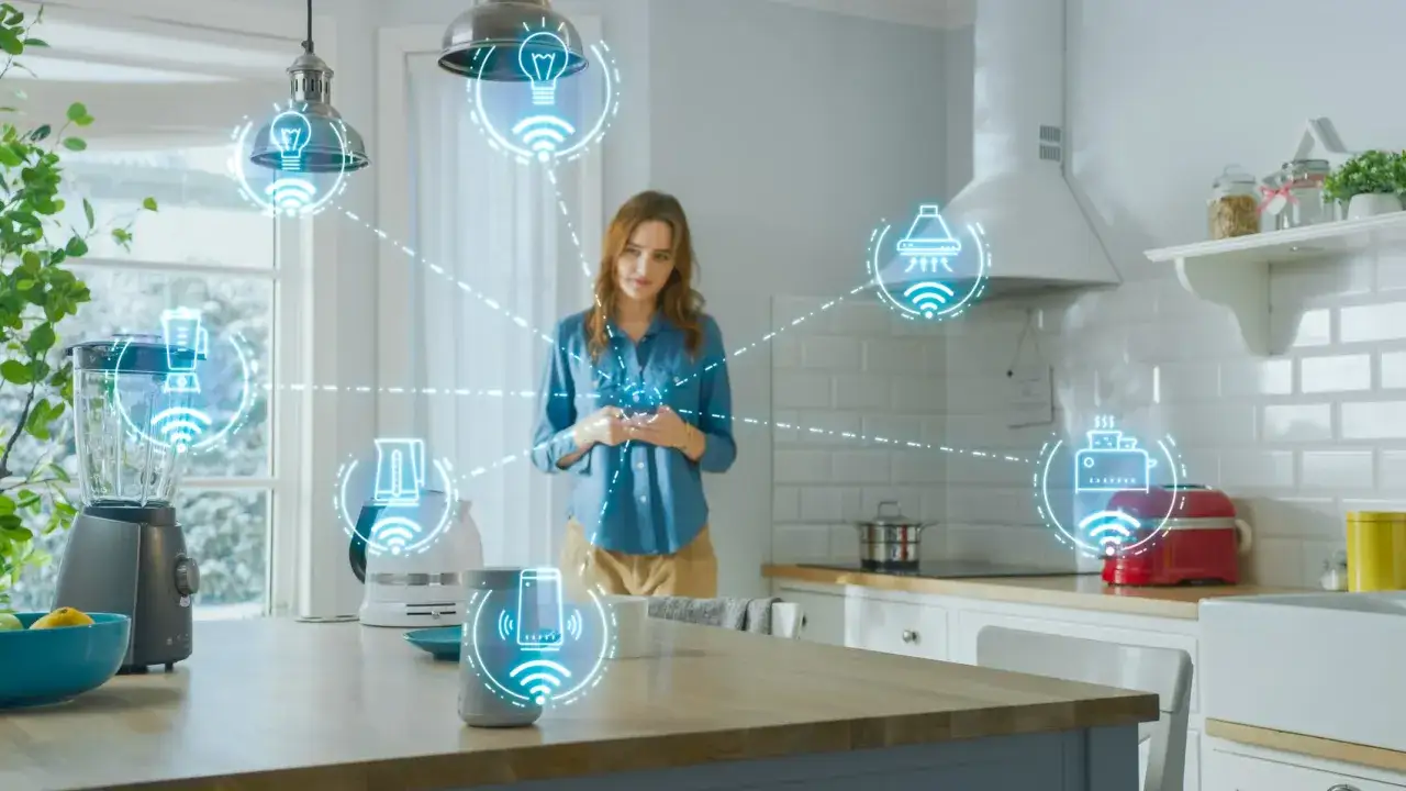 Mujer en cocina moderna interact&uacute;a con su m&oacute;vil, controlando electrodom&eacute;sticos conectados. Las ventajas de la dom&oacute;tica se visualizan con iconos de wifi y aparatos inteligentes.