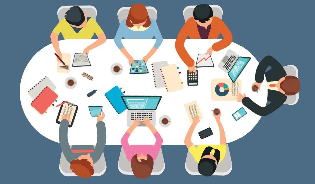 Teamwork im **extrem programming**-Stil: Leute arbeiten konzentriert an Tablets, Laptops und Notizbüchern an einem runden Tisch.