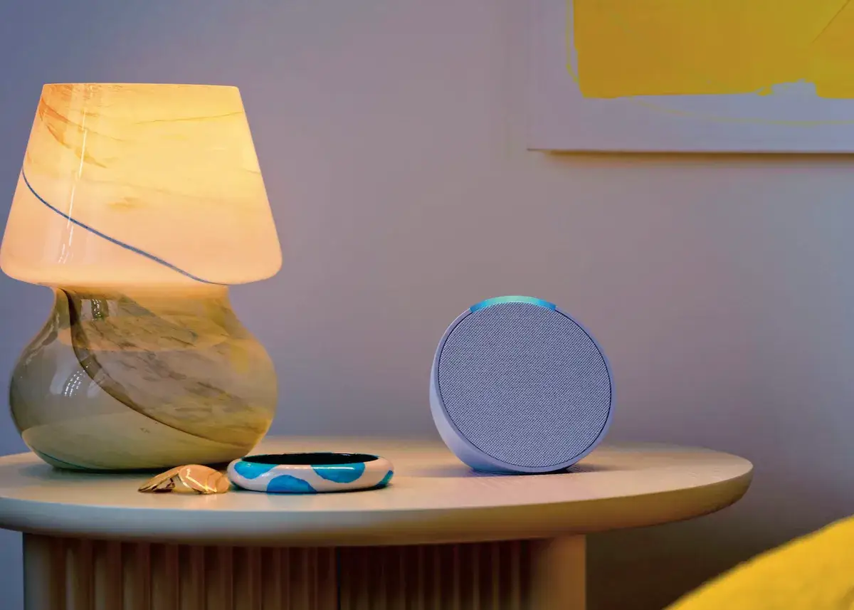 Okrągły głośnik z niebieskim podświetleniem, obok lampki i ozdób. Alexa język polski gotowa do pomocy.