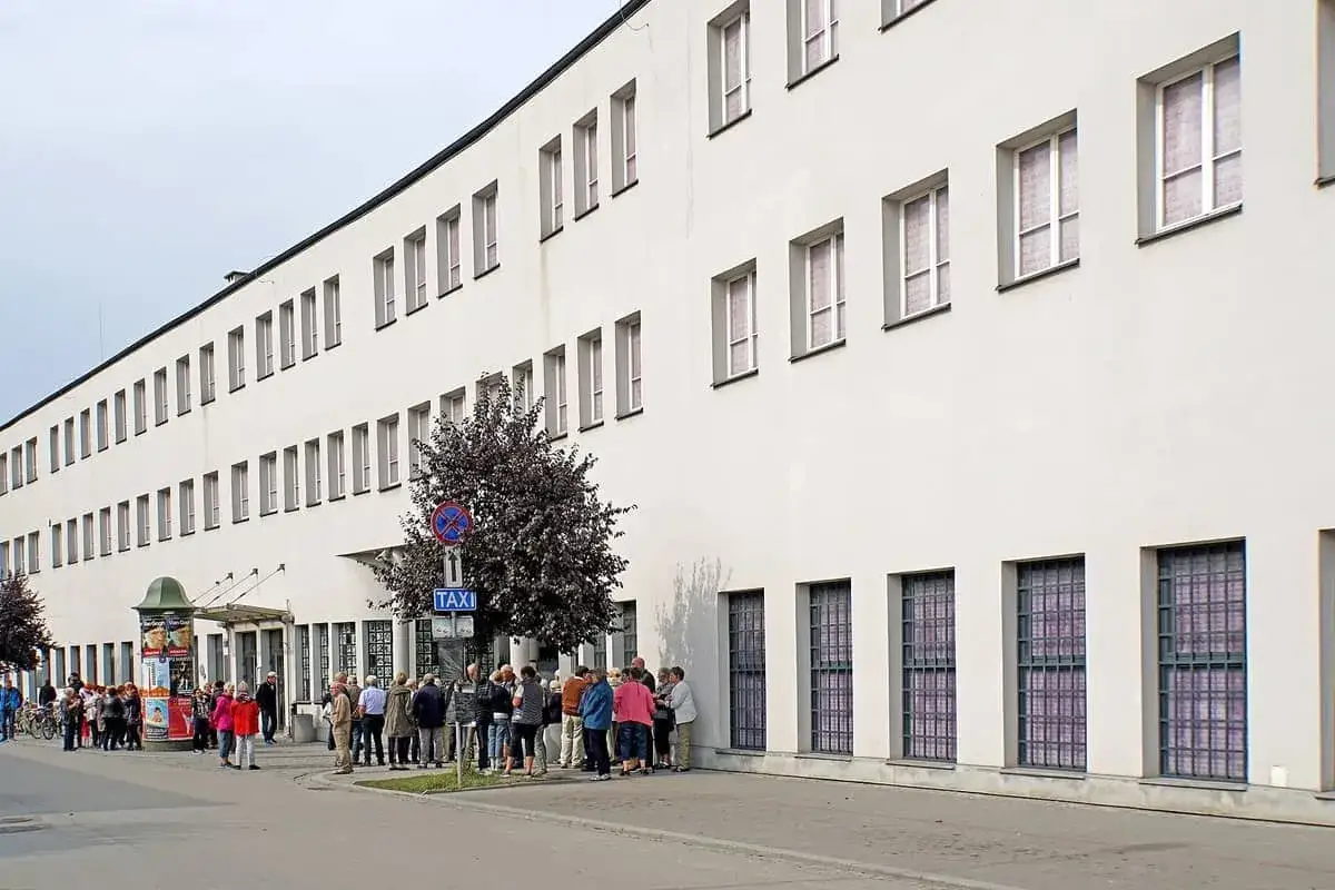 Bes&ouml;kare k&ouml;ar utanf&ouml;r Schindlers fabrik, en vit byggnad med m&aring;nga f&ouml;nster.