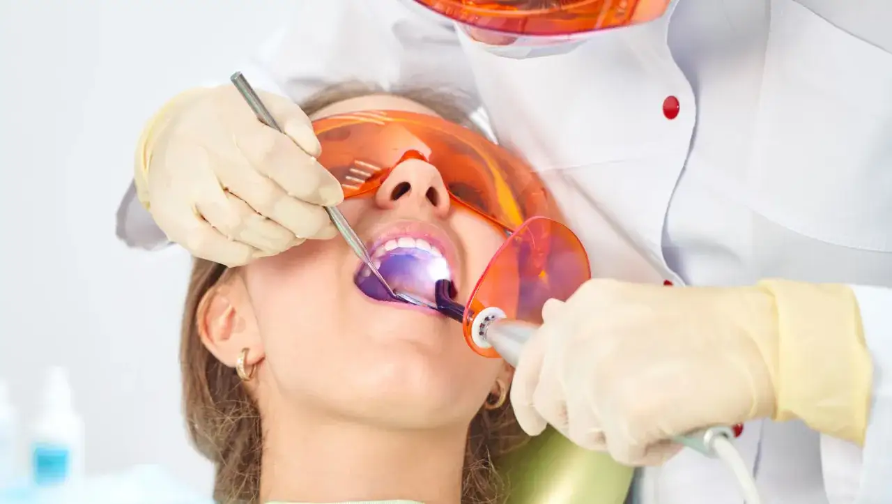 Dentysta utwardza światłem lampy nową plombę w zębie pacjentki.