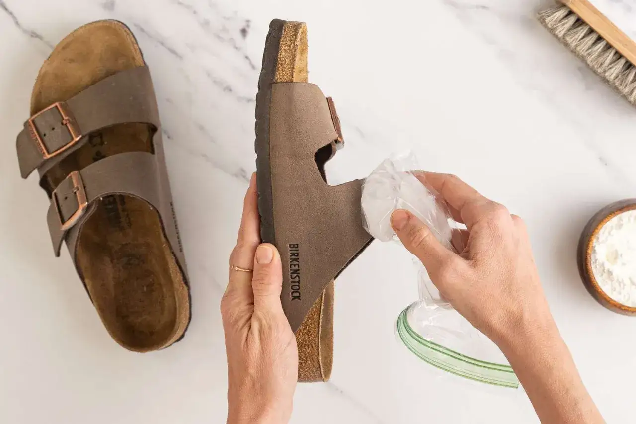 Jak czyścić Birkenstock? Delikatne czyszczenie brązowych sandałów Birkenstock za pomocą wilgotnej ściereczki. Obok leży szczotka i proszek.