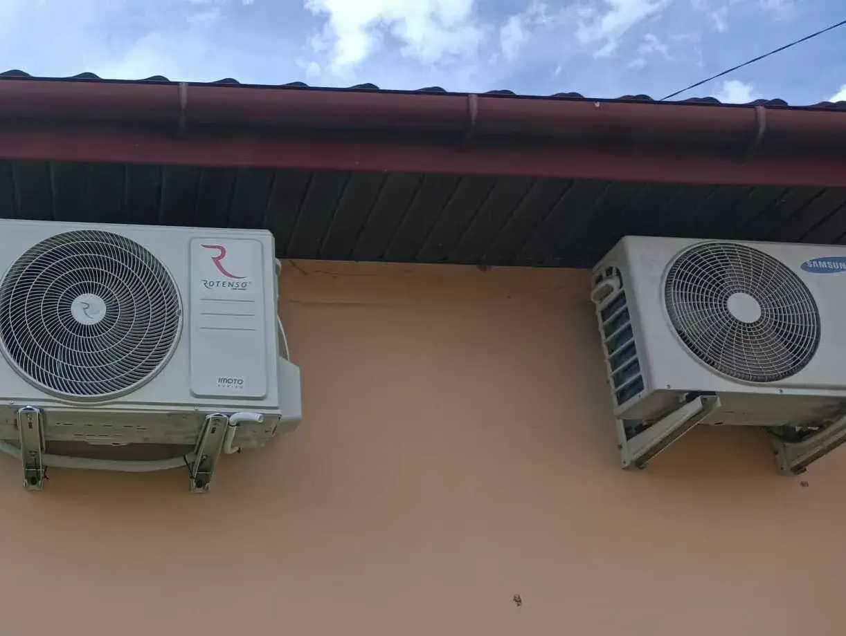 Dwa klimatyzatory zamontowane na ścianie budynku pod okapem dachu.