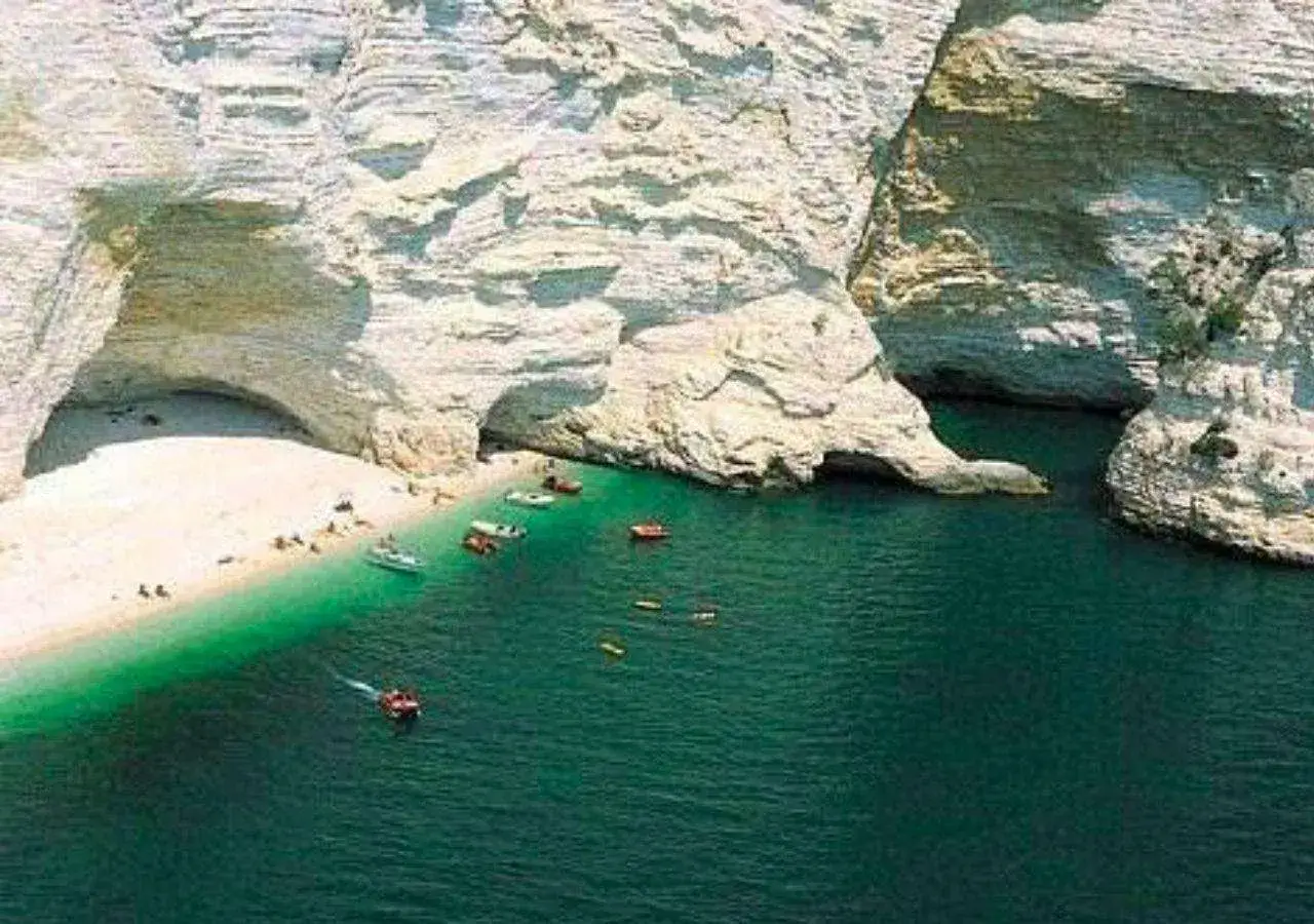 Spiagge di Manfredonia: sabbia bianca, acque cristalline e grotte naturali. Barche e bagnanti godono del sole in questo paradiso pugliese.