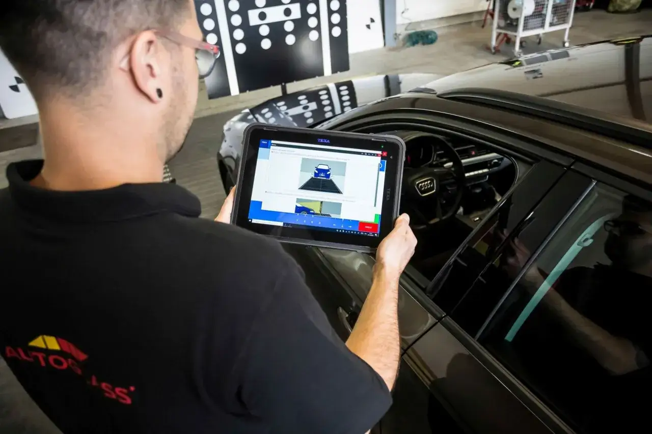Mechanik z tabletem w ręku monitoruje proces wymiany szyby w samochodzie. Na ekranie widoczny schemat pojazdu.