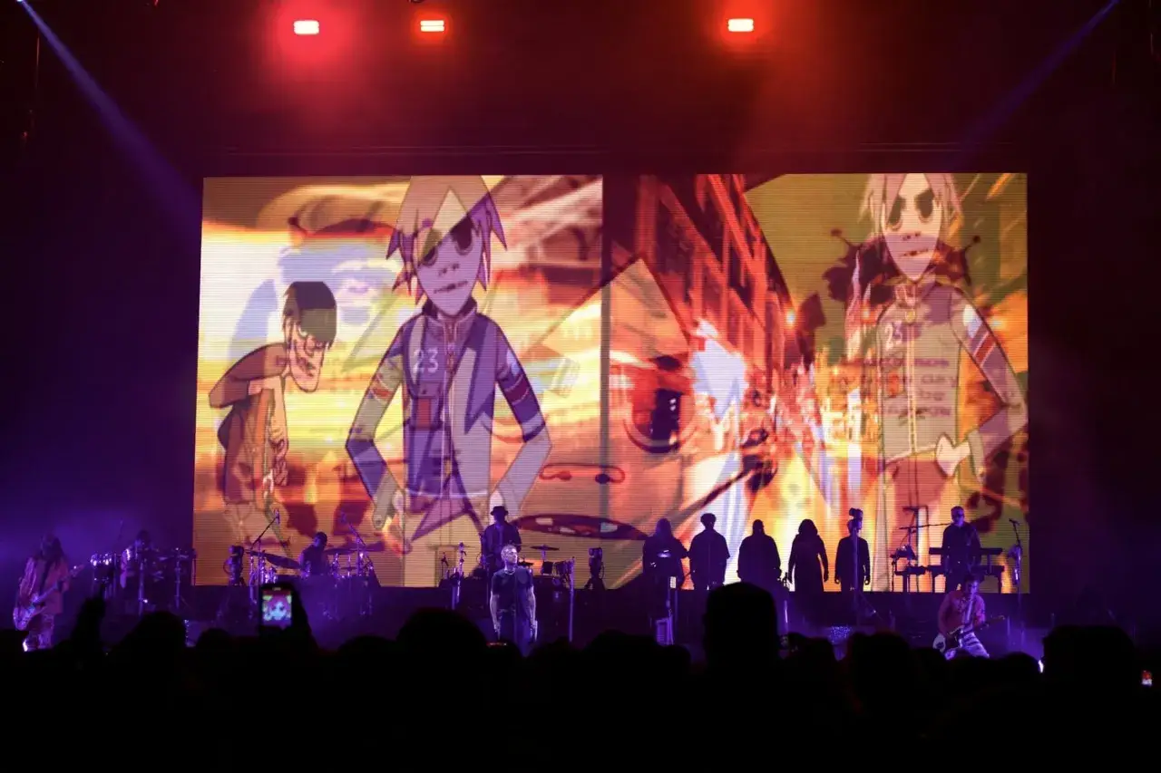 Gorillaz koncerty na żywo z animowanymi postaciami na ekranie. Widać zesp&oacute;ł na scenie i publiczność.