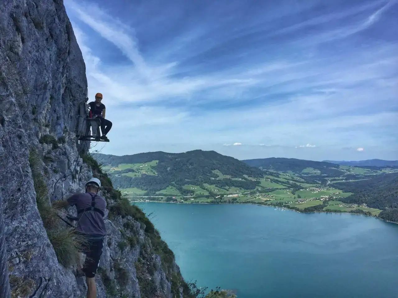 Kletterer am Felssteig der Drachenwand mit Blick auf den Mondsee und die umliegende Berglandschaft.