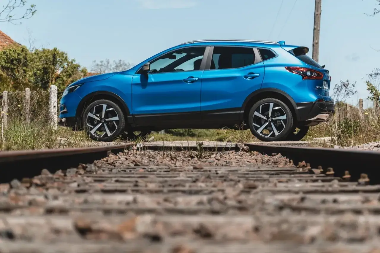 Un Nissan Qashqai bleu, aux dimensions parfaites pour l'aventure, est garé sur des voies ferrées désaffectées, prêt à explorer de nouveaux horizons.