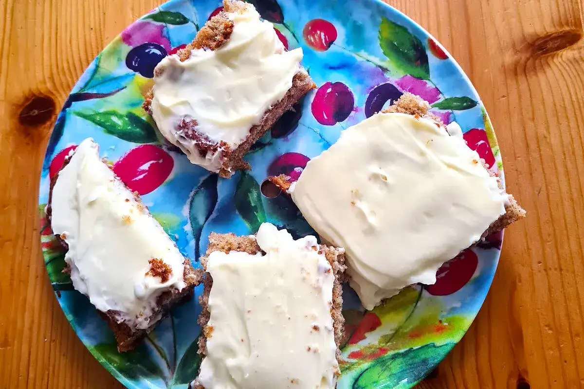Fyra bitar morotskaka med krämig frosting på en färgglad tallrik. Perfekt att frysa in morotskaka för senare njutning.