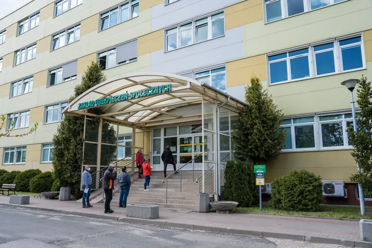 Ludzie stoją w kolejce przed budynkiem ZUS. Możliwe, że szukają informacji o ubezpieczeniu zdrowotnym ZUS dla niepracujących.