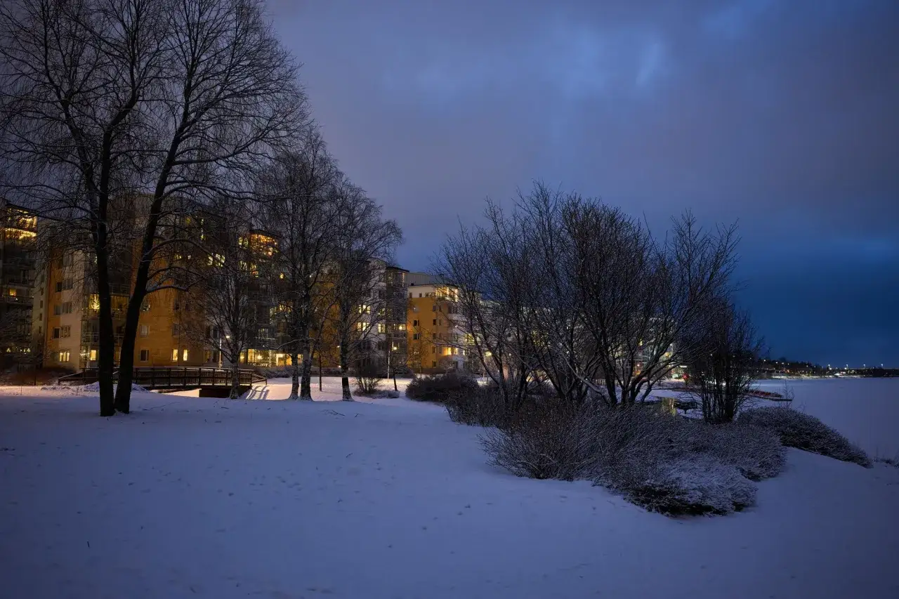 Vinterkv&auml;ll i Sverige med sn&ouml;, tr&auml;d och upplysta l&auml;genhetshus vid en frusen sj&ouml;. F&aring;ngat med en Ricoh GR IV.