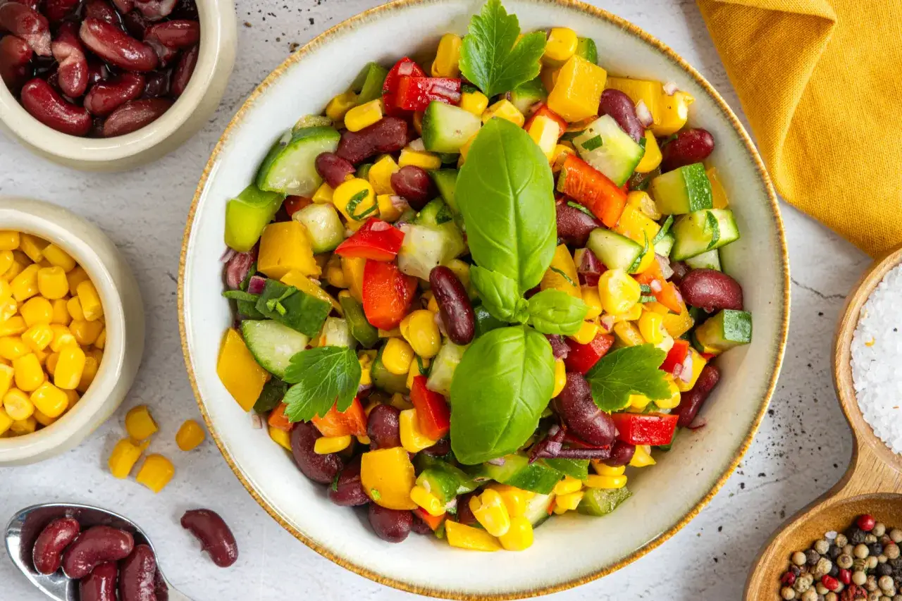 Bunter Kidneybohnen Salat mit Mais, Paprika und Gurke, garniert mit Basilikum.
