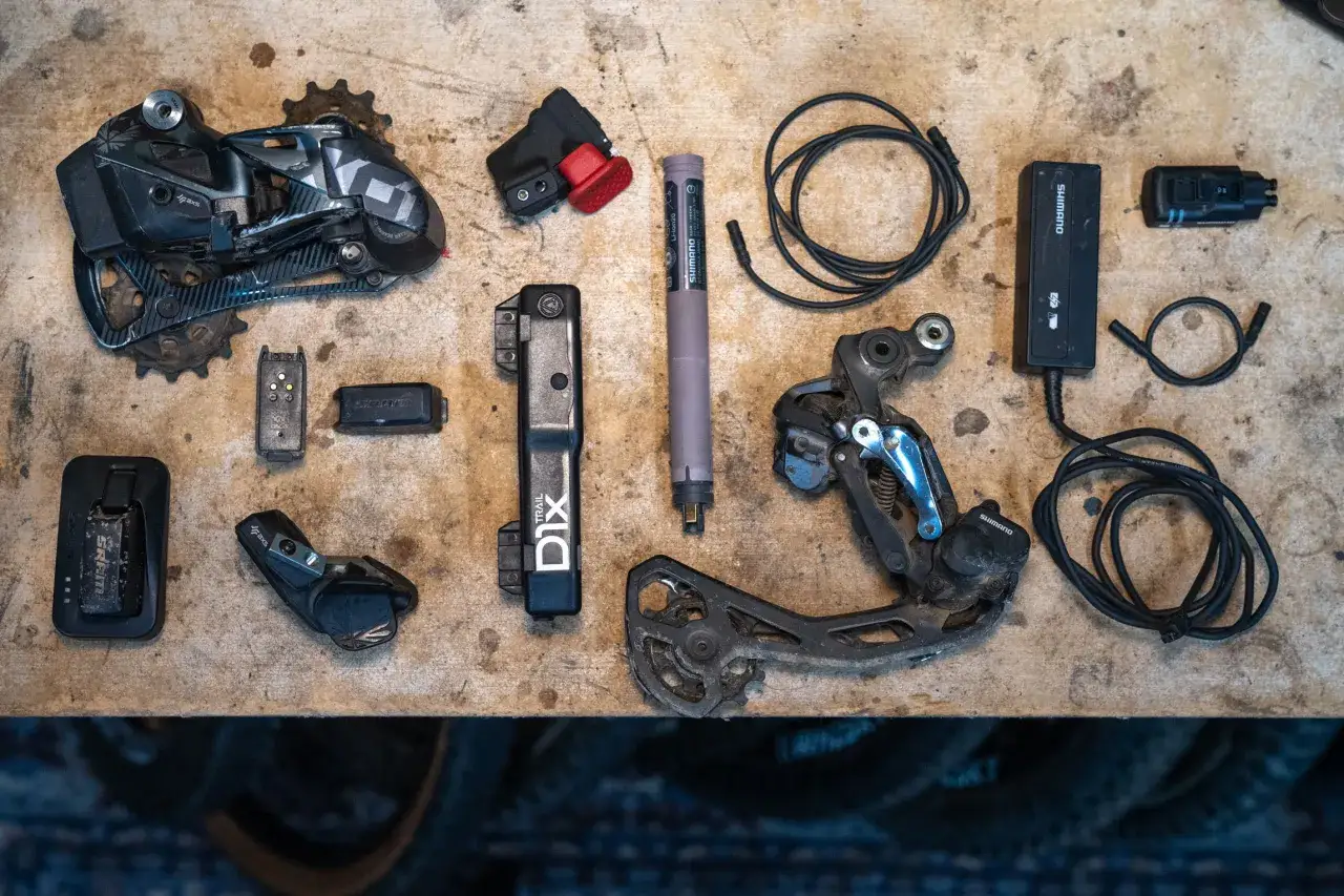 Comparing Shimano Di2 vs SRAM AXS electronic drivetrain components laid out on a workbench, ready for installation or maintenance.