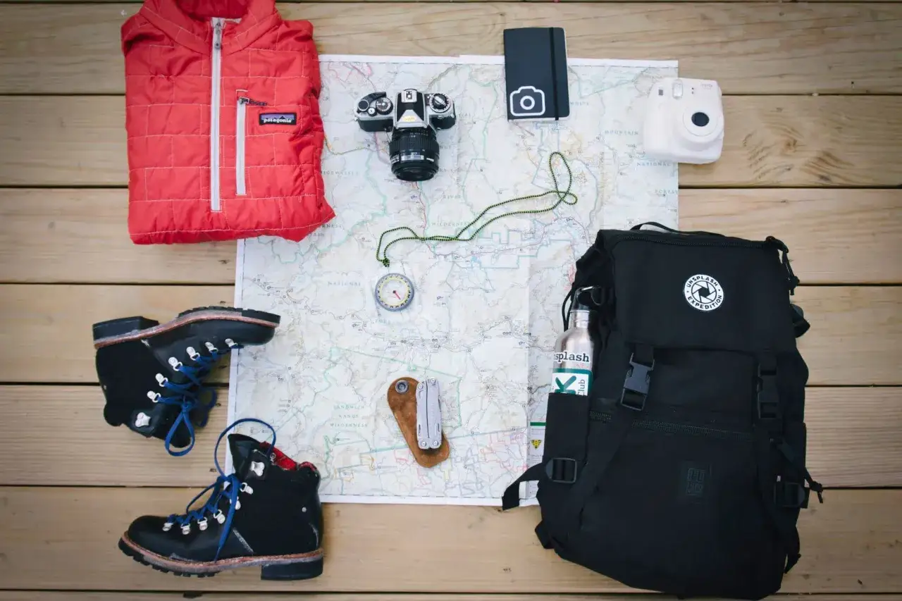 Packliste Kanada: Wanderschuhe, rote Daunenjacke, Kamera, Karte, Kompass, Multitool, Rucksack und Wasserflasche f&uuml;r das Abenteuer.