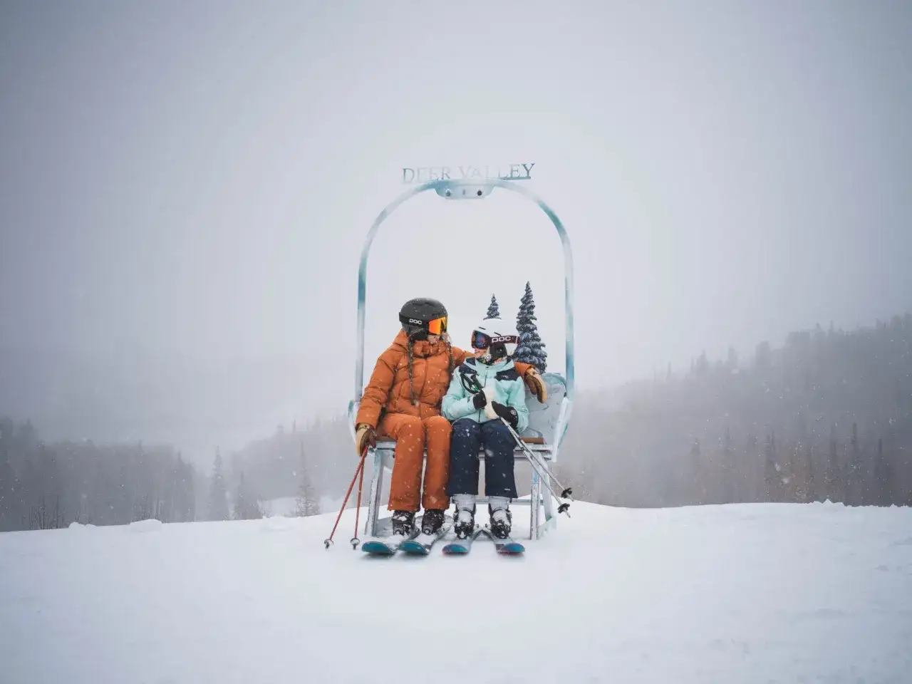 Para idealne miejsce, gdzie lecieć w grudniu: dwoje narciarzy siedzi na wyciągu krzesełkowym w Deer Valley, otoczeni śniegiem i lasem.