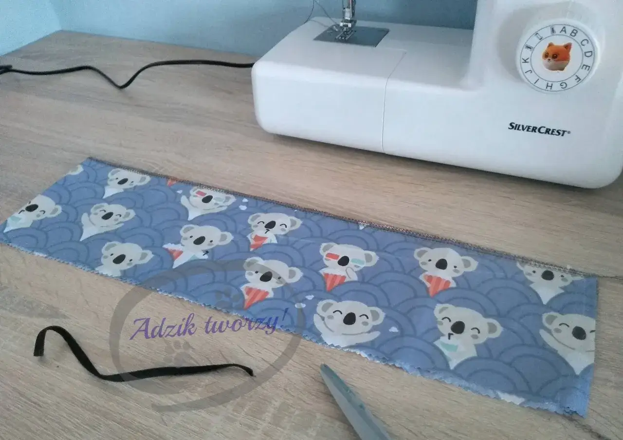 Tkanina z motywem misiów koala i gumka do włosów czekają na to, jak uszyć scrunchie. Maszyna do szycia SilverCrest w tle.