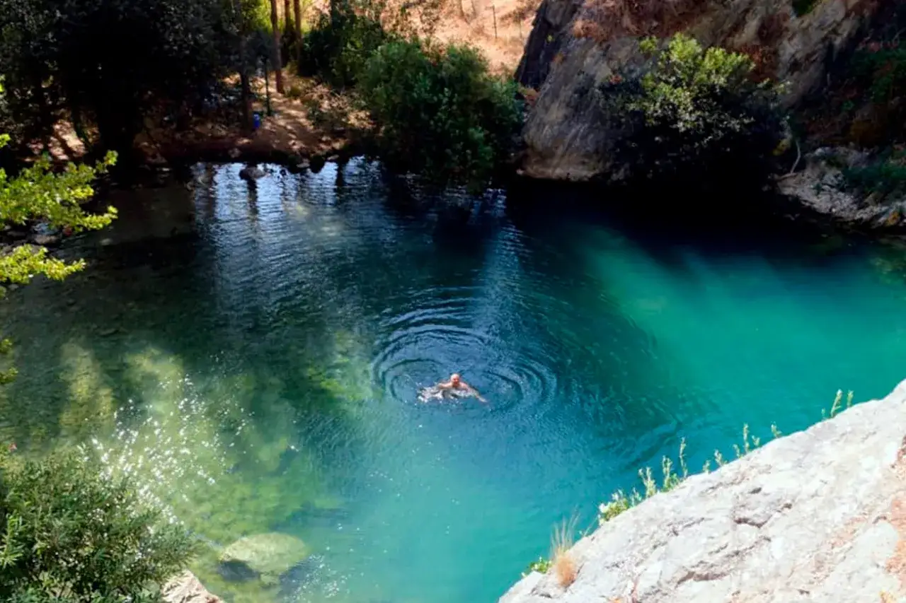 Un hombre disfruta ba&ntilde;arse en la cueva del gato, un oasis de aguas turquesas rodeado de vegetaci&oacute;n y rocas.