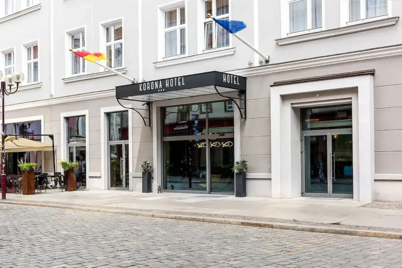 Elegancki hotel Korona Wrocław z charakterystycznym czarnym zadaszeniem nad wejściem. Flagi powiewają na wietrze.
