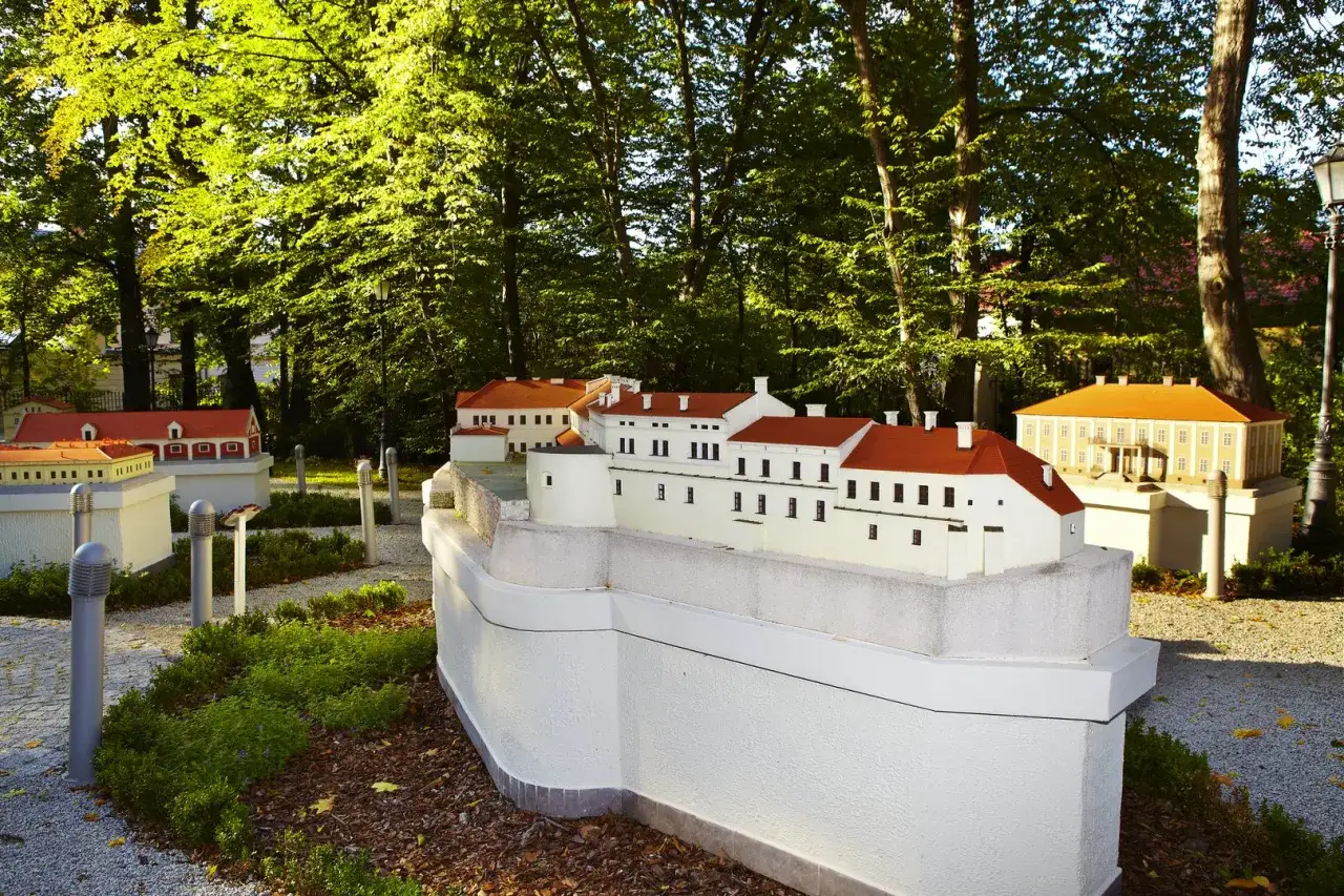 Miniatury budynków w parku w Żywcu. Widać białe budowle z czerwonymi dachami, otoczone zielenią i drzewami.