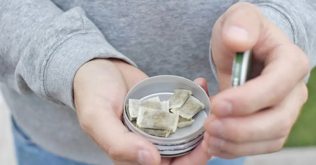 Osoba trzyma puszkę z kilkoma woreczkami. To jest snus, tytoń do ust.