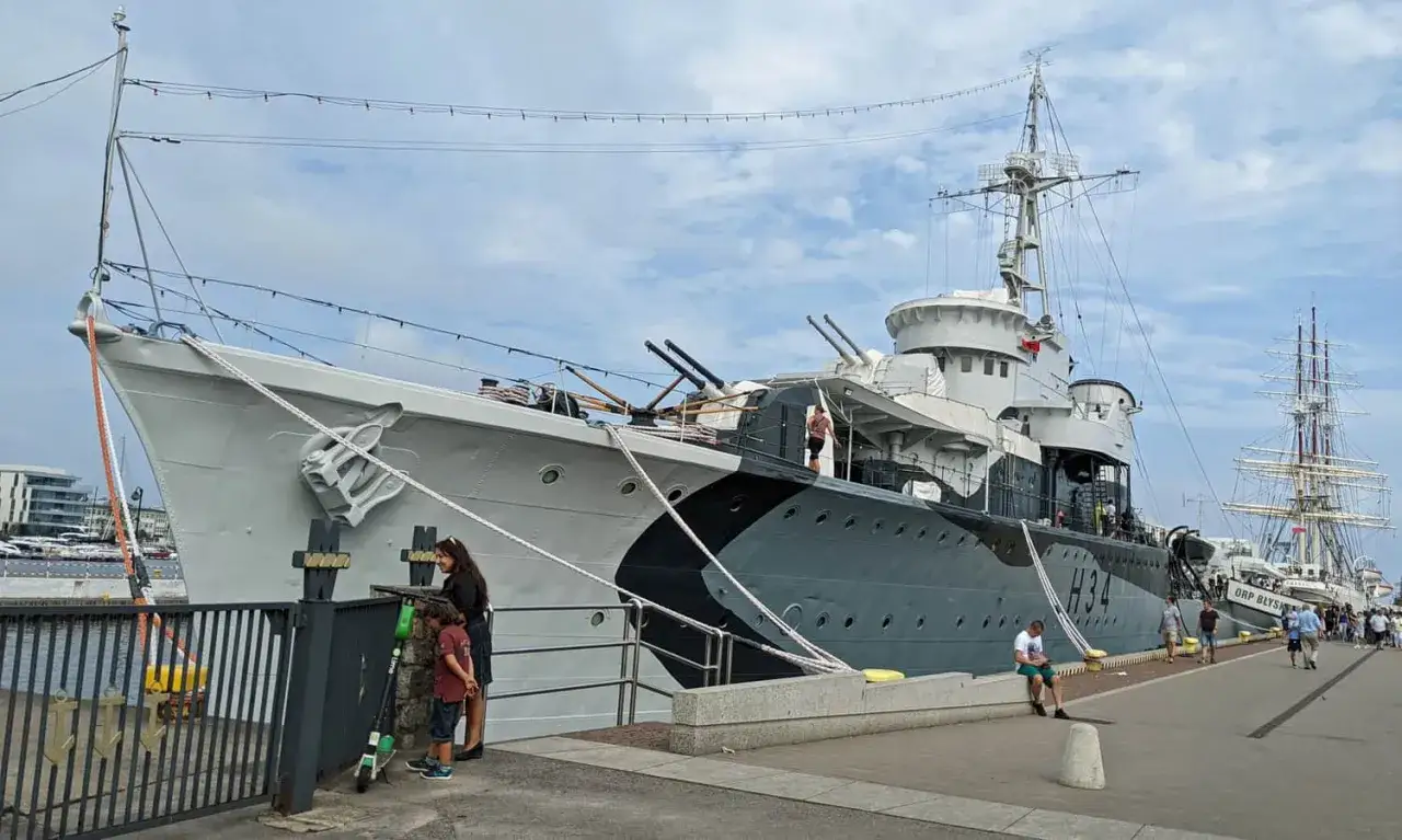 ORP Błyskawica, historyczny niszczyciel, cumuje przy nabrzeżu. Obok widać żaglowiec.