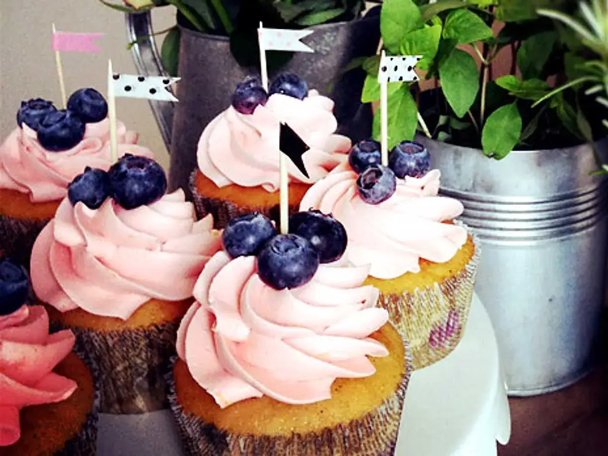 Sju muffins med rosa frosting och bl&aring;b&auml;r, dekorerade med sm&aring; flaggor. Perfekt f&ouml;r ett sommarfika!