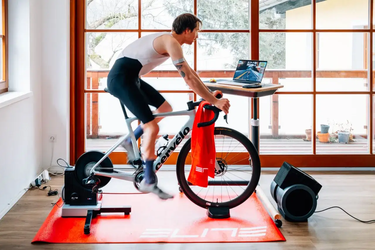 Man cycling indoors, following virtual routes on a laptop, part of his indoor bicycle training programs.