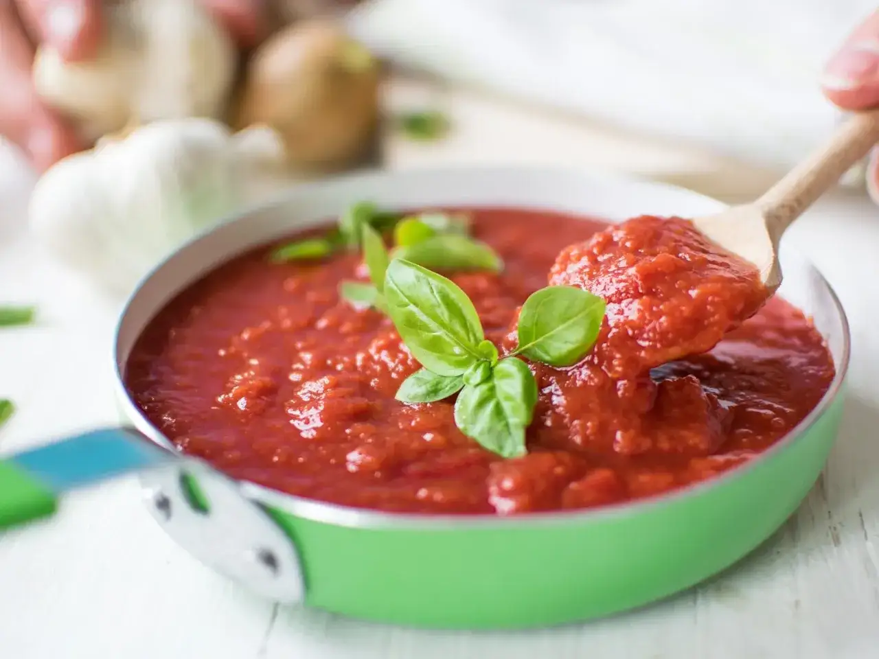 Sos pomidorowy ze świeżych pomidorów, z bazylią, w zielonej patelni. Na łyżce porcja aromatycznego sosu.