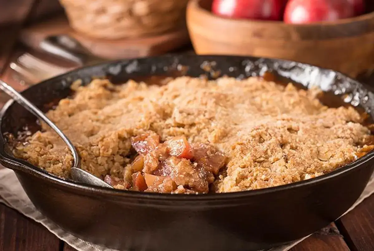 Un d&eacute;licieux crumble aux pommes, parfait pour une recette Cyril Lignac. La cuill&egrave;re attend de servir cette gourmandise dor&eacute;e.