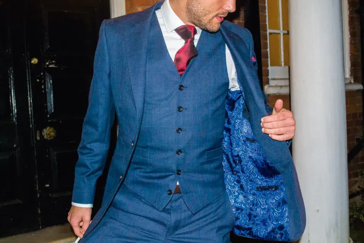 A man in a blue plaid suit, showing the proper way to button a vest: leave the bottom button undone. The suit has a vibrant paisley lining.
