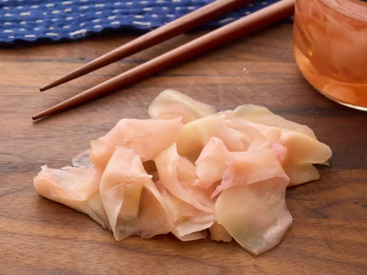 Różowy imbir do sushi, pałeczki i słoiczek z marynatą na drewnianej desce.