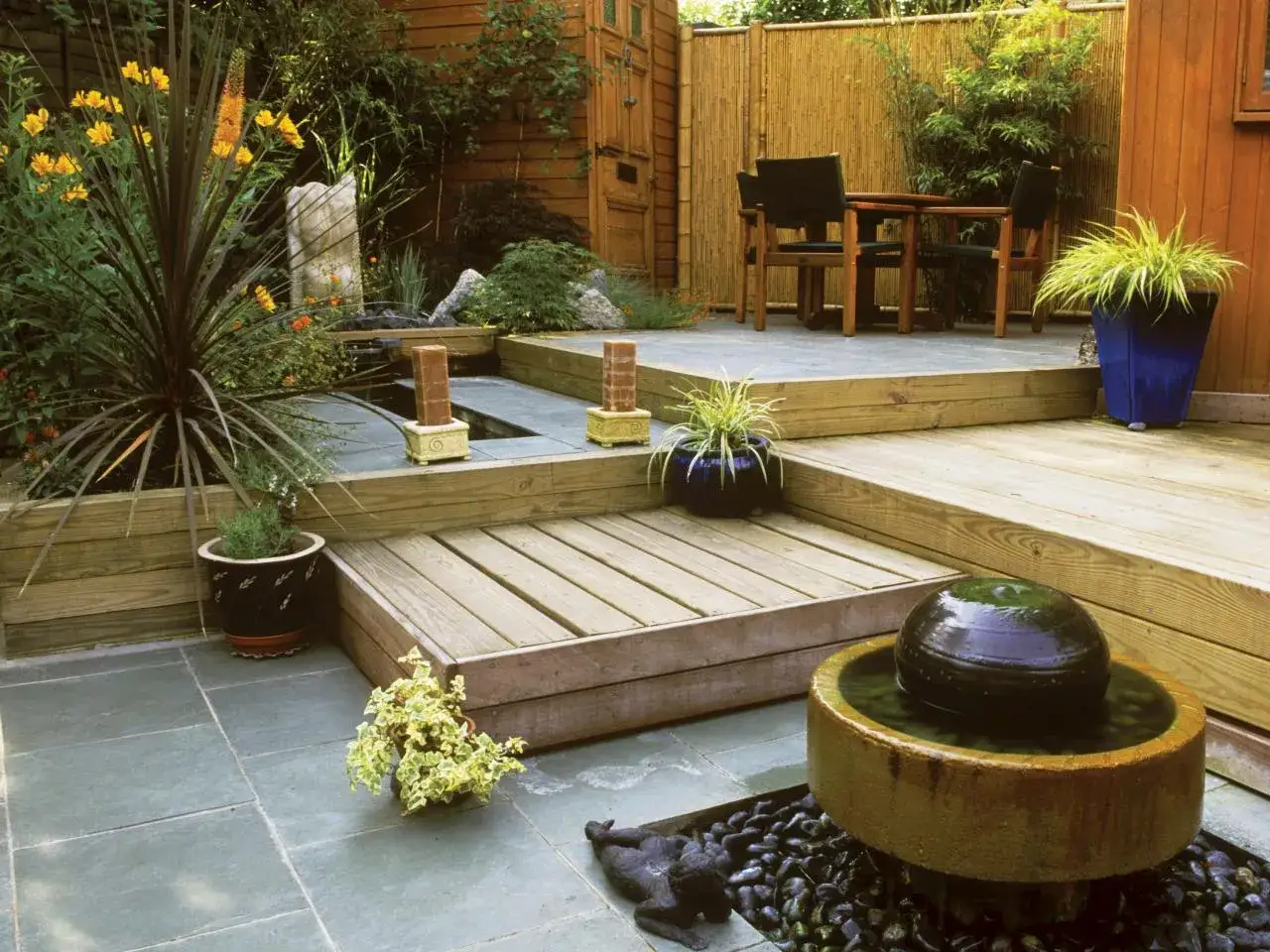 Un **mini jard&iacute;n japon&eacute;s en casa** con estanque, fuente de agua, plantas exuberantes y una zona de estar de madera.